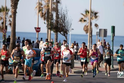 Corredores del Medio Maratón 2024 en el paseo marítimo de Almería, apoyados por el público bajo el sol