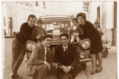 Francisco Hernández, agachado en cuclillas, con un cigarro en la mano, junto a unos clientes. Al lado se ve un antiguo surtidor de gasolina.