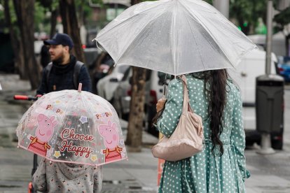 Una mujer y su hija, con un paraguas en un día de lluvia.