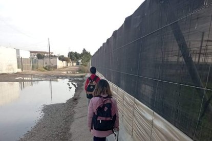 Una familia sobre un bordillo para poder cruzar un camino de Los Grillos a Los Nietos en Níjar.