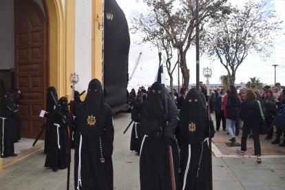 Un nazareno con capuz portando la bandera de la hermandad, negra y blanca.