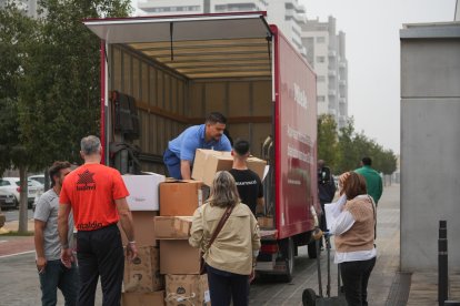 Varias personas llevan cajas con mantas, ropas y objetos de primera necesidad para las personas que se encuentran en el pabellón de baloncesto.