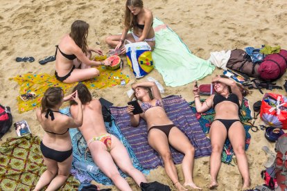 Unas chicas toman el sol en la playa, sin sombrilla.