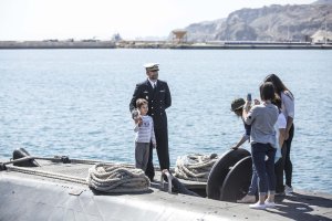 Un miembro de la tripulaición posa con visitantes al submarino.