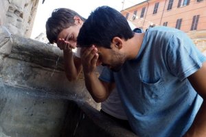 Dos chicos mojan su cara en una fuente para combatir las altas temperaturas.