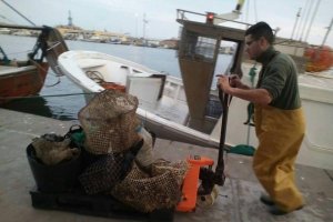 Un pescador  empujando basura y nasas recogidas del fondo del mar hace unas semanas