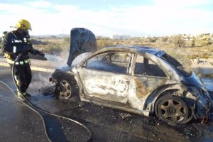 Un bombero termina de enfriar el coche incendiado.