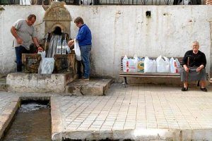 Personas llenando botellas en la Fuente del Oro, mientras espera su turno una vecina.