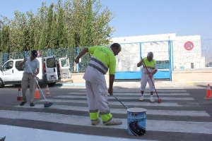 Operarios municipales repintan un paso de peatones frente a un colegio del municipio.