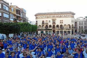 Cientos  de mayores hacen gimnasia sentados en la plaza del pueblo.tyle>.apqj{position:abs