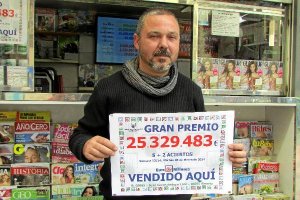 El quiosquero  Juan Carlos Andújar Lazo posa junto al cartel que anuncia la cifra del premio que ha 