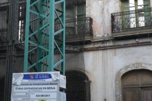 Grúa ante la fachada del edificio en la que se puede ver el cartel con datos de la obra.