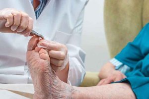 Podólogo cortándole las uñas a un anciano en una consulta.