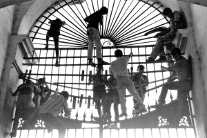 un grupo de muchachos escalando por las rejas de la Plaza de Toros en busca de un resquicio por donde poder colarse.