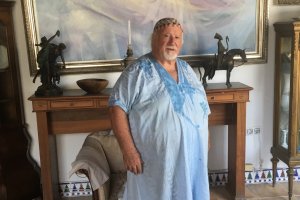 Manolo Coronado con su túnica azul, bajo uno de sus cuadros, en su casa de la montaña.