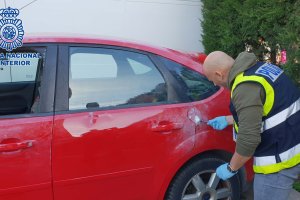 Un agente buscando huella en el exterior de un vehículo.