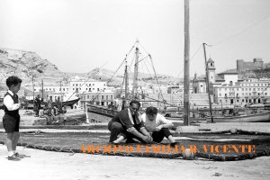 Un pescador mostrando los secretos de remendar las redes a unos paseantes en una mañana de domingo (Años 50).