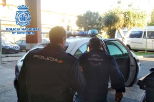 Un agente, conduce al detenido hasta un vehículo de la Policía Nacional.