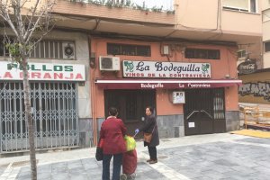Dos señoras saludándose en la calle Trajano. Parecen estar poniéndose al día, cargadas de alimentos, frente a la Bodeguilla y Pollos La Granja.