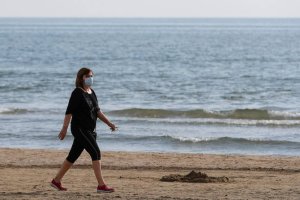 Una mujer con mascarilla pasea por la playa de la Malvarrosa / Iván Terrón.