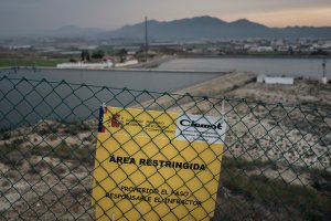 Vala que acota el área contaminada, con el puerto al fondo.
