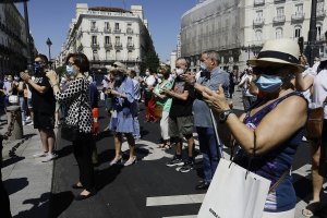 Transeúntes aplauden al finalizar el minuto de silencio en memoria por los fallecidos por el COVID-19 en Madrid.