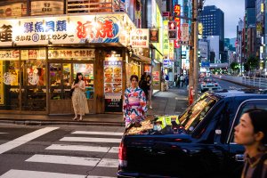 Intersección de calles repleta de luminosos mientras una joven con kimono cruza un paso de cebra (Foto: Chema Artero).