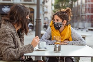 Dos mujeres toman café con mascarilla en una terraza.