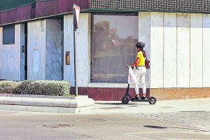 Imagen de archivo de una mujer utilizando un patinete eléctrico por la acera.
