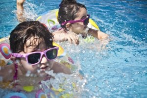 Dos niños equipados con flotadores y gafas de sol juegan en una piscina.