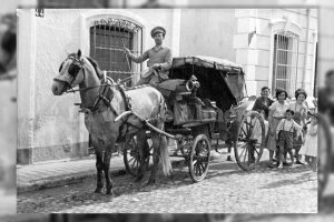 Un grupo de niños y jóvenes del Barrio Alto tratando de subirse a la tabla trasera de un coche de caballos. Años 50.
