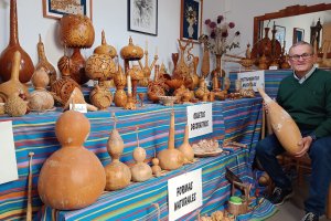 Manuel Ayala posa con su colección de tallas de calabazas desplegada en el salón de su casa.