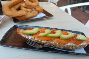 Tostada de salmón marinado y aguacate. Detrás media ración de churros.