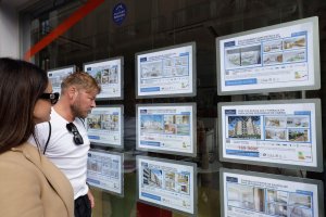 Ciudadanos observando ofertas de pisos en una oficina inmobiliaria.