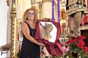 Emilia Resina Portaz muestra la pintura donada para el nuevo estandarte de la Cofradía junto a la imagen del Santísimo Cristo del Bosque, en Bacares.