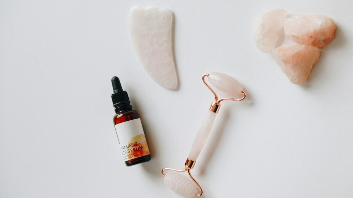 Aceite limpiador facial junto a un rodillo y una piedra gua sha para el cuidado de la piel.