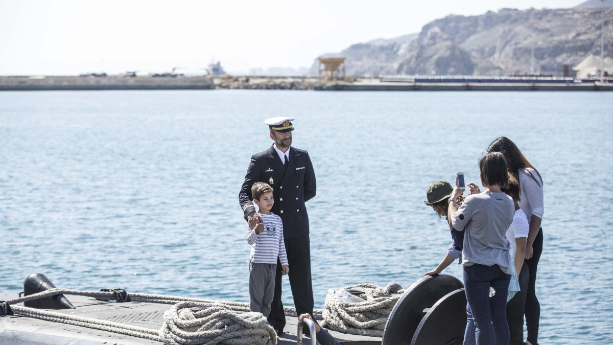 Un miembro de la tripulaición posa con visitantes al submarino.