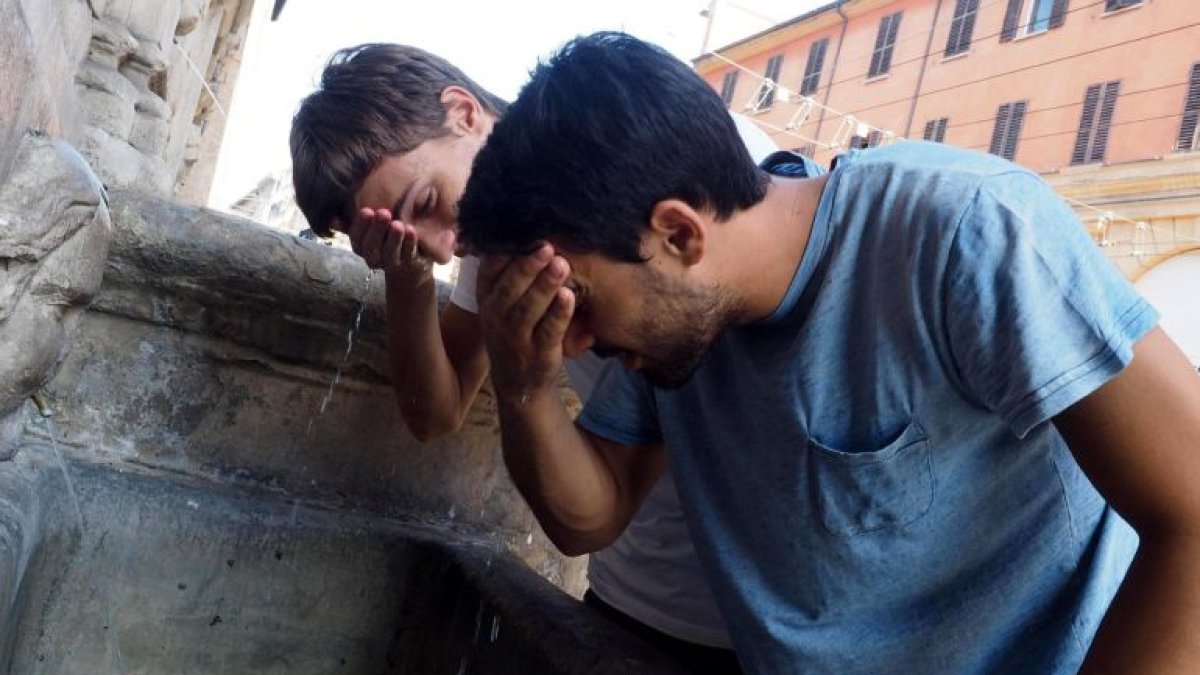 Dos chicos mojan su cara en una fuente para combatir las altas temperaturas.