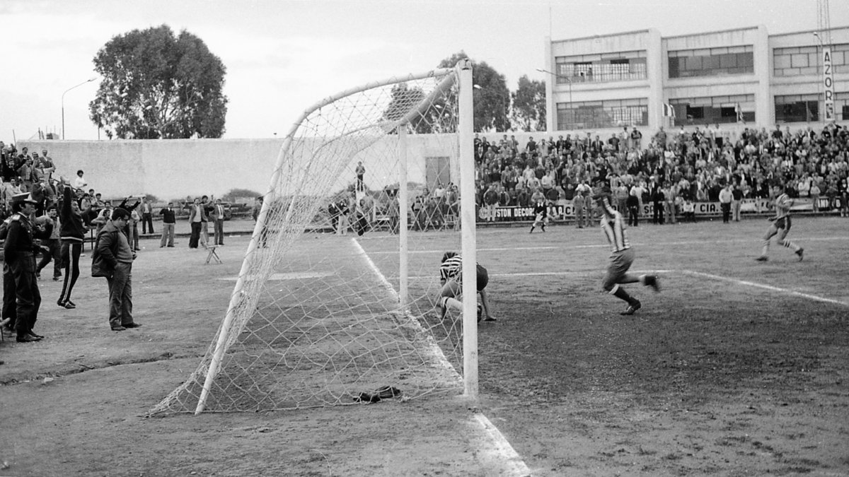 Rafaelico Andújar detrás de la portería, asistiendo con tranquilidad, con las manos en los bolsillos y mirando por encima de las gafas, a un gol del
