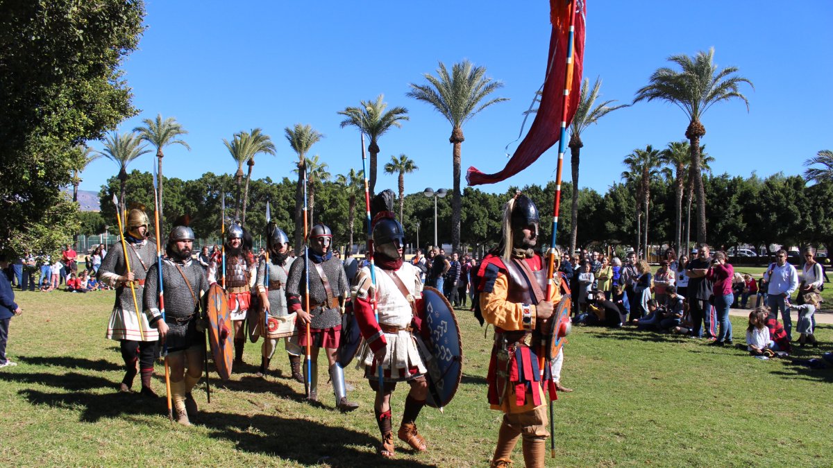 Soldados desfilando y recreando batallas y formaciones militares en el parque municipal acompañados en el otro extremo por diversos personajes de una