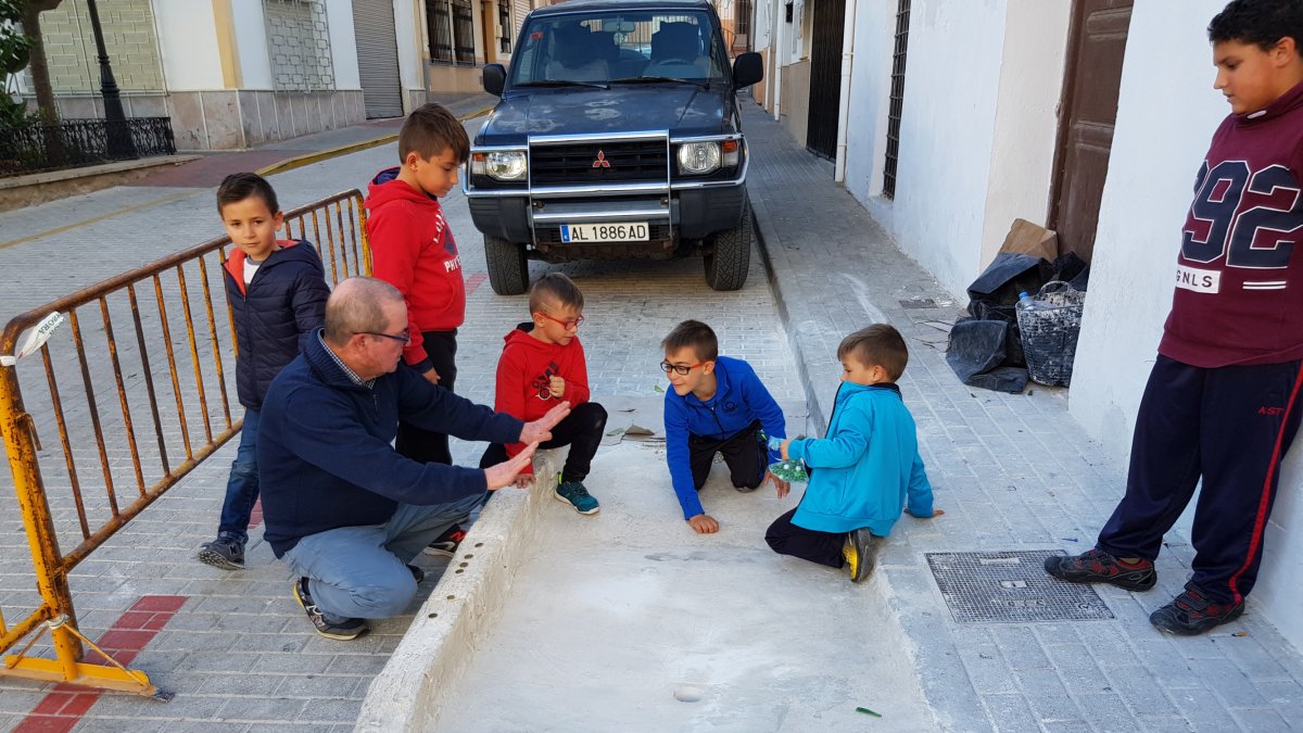 El abuelo enseña a los nietos cómo se juega al boliche.
