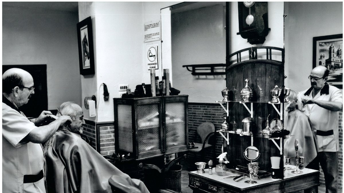 Imágenes de la barbería Mora con José Mora atendiendo a un cliente (arriba) y el estado actual, deshabitado por cierre, de la barbería (abajo).