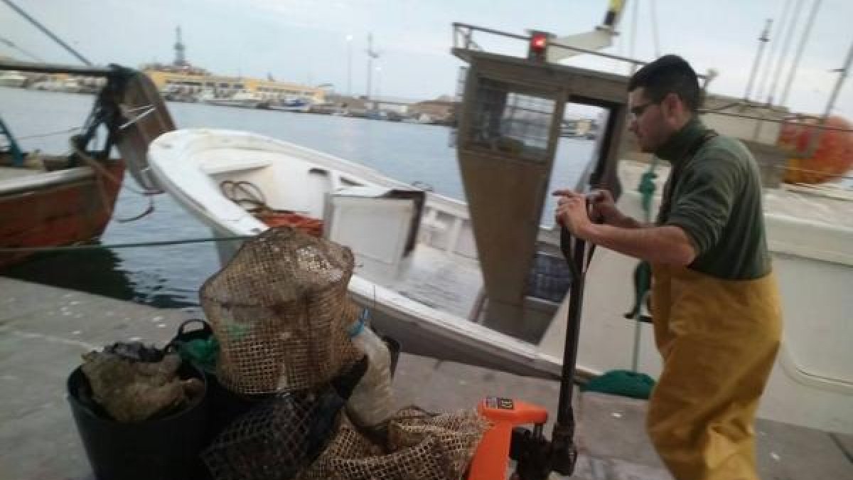 Un pescador  empujando basura y nasas recogidas del fondo del mar hace unas semanas