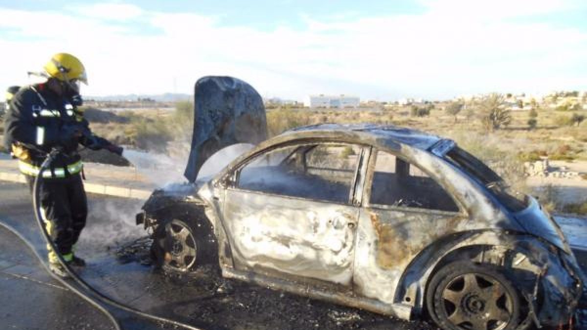 Un bombero termina de enfriar el coche incendiado.