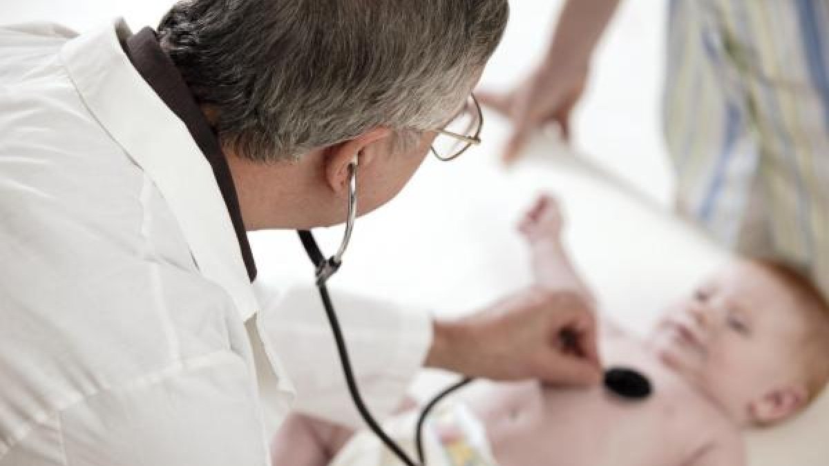 Un médico ausculta a un bebé en una consulta.