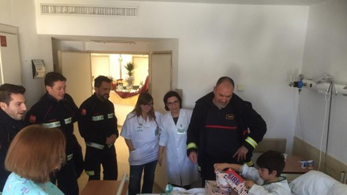 Un niño abre los regalos en presencia de algunos bomberos.