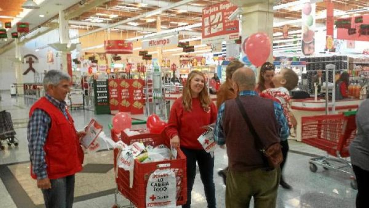 Un abuelo con su nieta conversa con dos voluntarios de Cruz Roja en Alcampo.