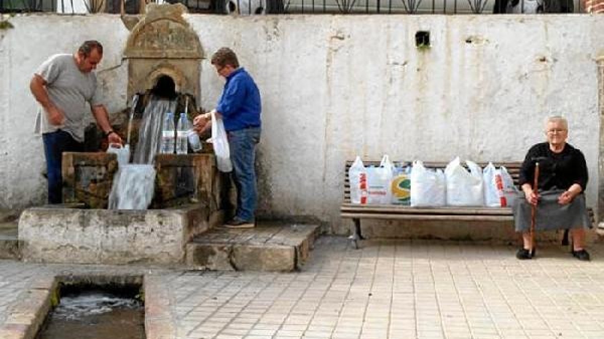 Personas llenando botellas en la Fuente del Oro, mientras espera su turno una vecina.