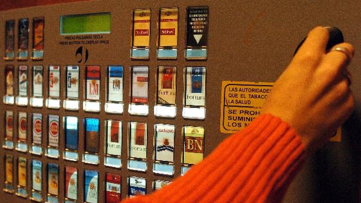 Una persona saca tabaco de una máquina expendedora.
