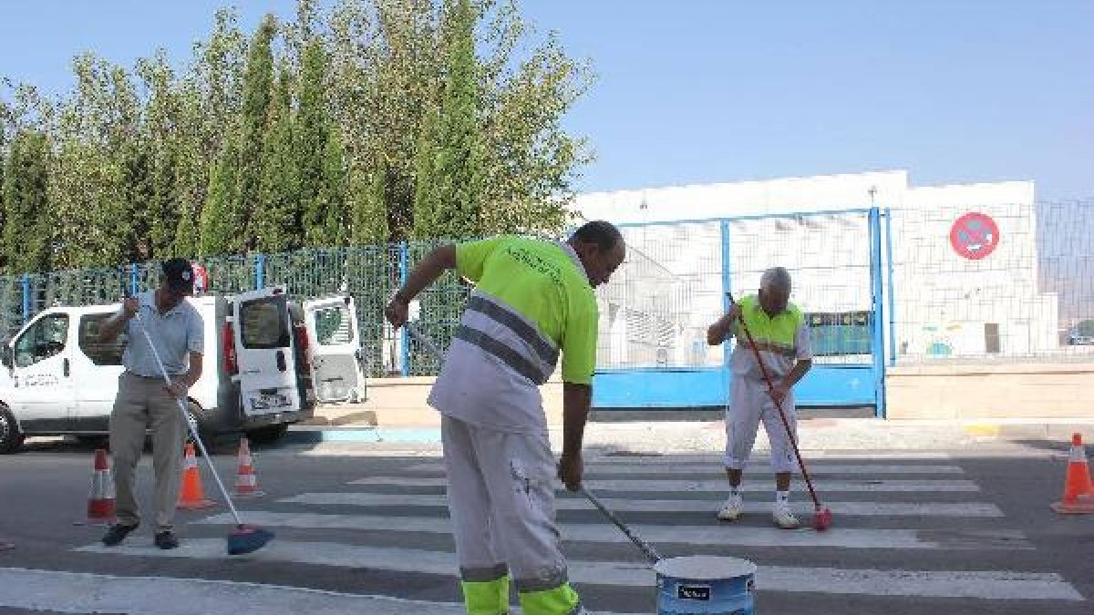 Operarios municipales repintan un paso de peatones frente a un colegio del municipio.